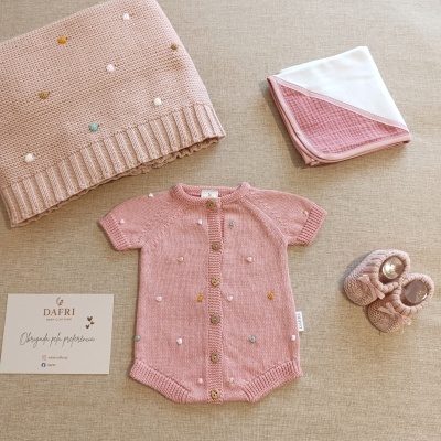 Conjunto de roupa e acessórios de bebé em tons cor de rosa com manta e sapatos em fundo bege