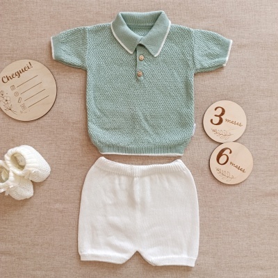 Conjunto de roupa de bebé em malha verde água e branco com sapatinhos e placas de madeira.