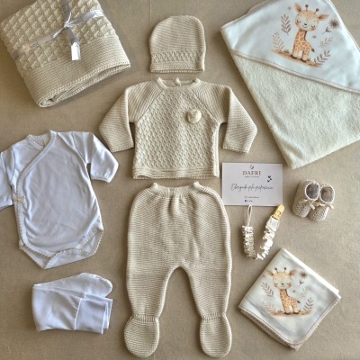 Conjunto de bebé em malha bege com body branco, manta com estampa de girafa, babete, patucos e cartão DAFRI sobre superfície bege