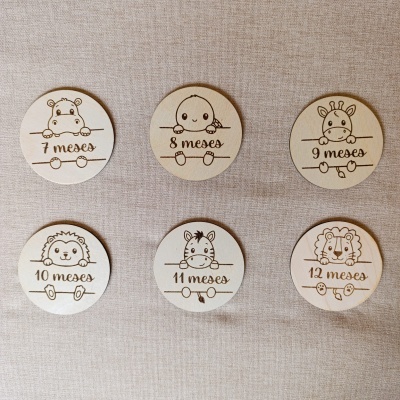 Tarecos circulares de madeira com desenhos de animais e texto de meses para bebés sobre tecido bege.