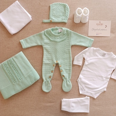 Conjunto de roupa de bebé verde clara e branco com manta e sapatinhos sobre fundo castanho claro