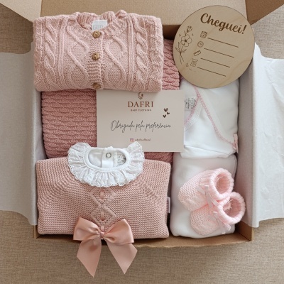 Conjunto de roupa de bebé rosa e branca em caixa com cartão e placa de madeira