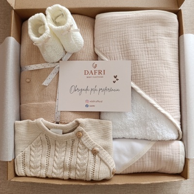 Conjunto de roupa de bebé em tons neutros dentro de caixa de cartão.