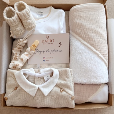 Conjunto de roupa de bebé em cores neutras numa caixa com body, bata, meias e manta da marca DAFRI