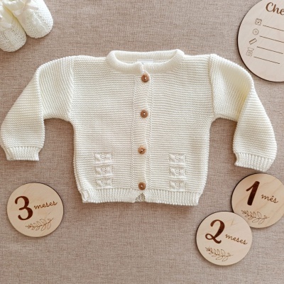 Casaco branco de malha para bebé com botões de madeira e discos de madeira com meses.