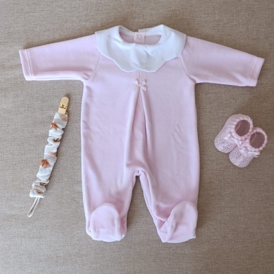 Conjunto para bebé rosa com body, chupeta e sapatinhos sobre superfície bege