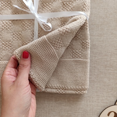 Manta bege de malha com padrão texturizado e fita branca