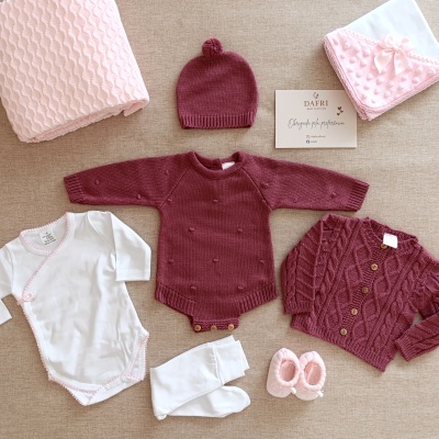 Roupa de bebé com body branco, casaco vinho, tapa-fraldas vinho, touca vinho, meias brancas, sapatinhos rosa, manta rosa e capuz branco com bolinhas rosa.