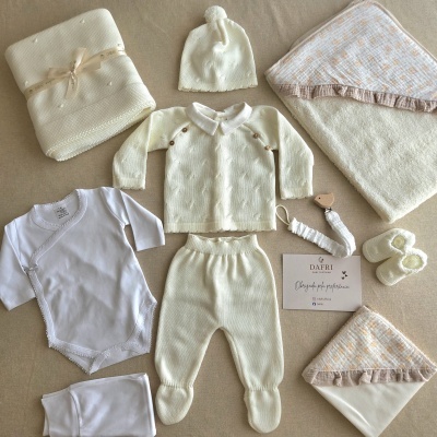 Conjunto de roupa e acessórios de bebé em tons creme e branco sobre superfície bege