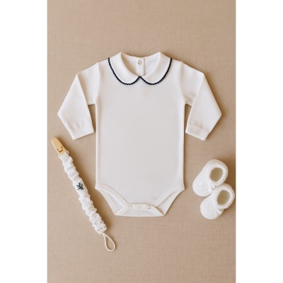 Conjunto de roupa de bebé branca com gola preta, chupeta com correia e sapatinhos de lã