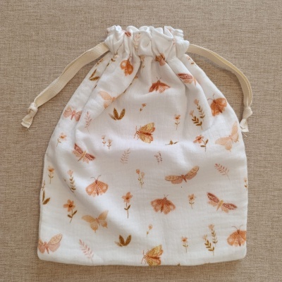 Saco de pano branco com padrão de borboletas e flores em tons de laranja e castanho claro