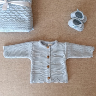 Conjunto de bebé azul claro com casaco, sapatinhos e manta sobre superfície bege