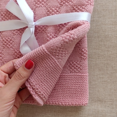 Manta ou roupa de bebé rosa em malha com laço branco sobre superfície bege