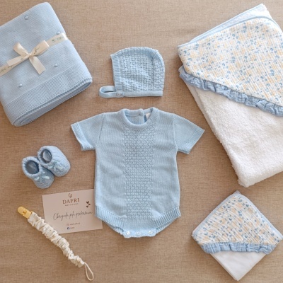 Conjunto de roupa e acessórios de bebé em azul claro sobre superfície bege.