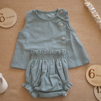 Conjunto de roupa para bebé azul clara com botões e laço, sapatinhos brancos e discos de madeira com indicações de idade em meses