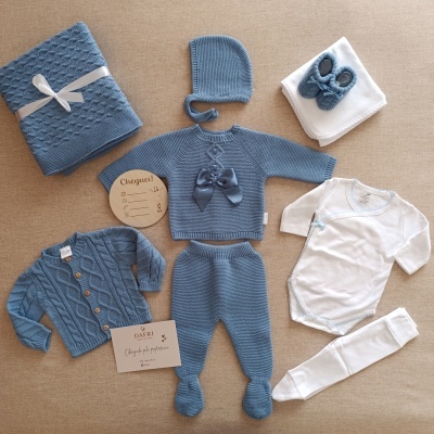 Conjunto de roupa de bebé azul e branco com vários itens dispostos sobre fundo bege.