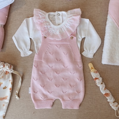 Macacão bebé rosa em malha fina com body branco e gola babado rosa sobre fundo bege