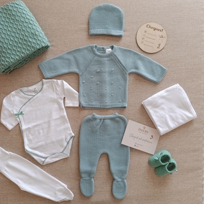 Conjunto de roupa de bebé com casaco azul claro, body branco, calças, gorro e sapatinhos, mantas e placa de madeira