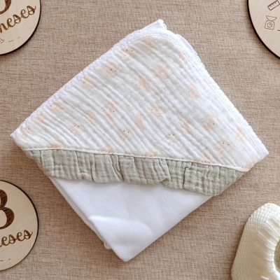 Fralda branca com padrão e borda bege sobre tecido castanho claro com discos de madeira