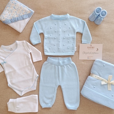Conjunto de roupa de bebé azul e branco com manta, body e sapatinhos, sobre superfície bege