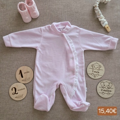Conjunto de bebé rosa com botinhas e discos de madeira em fundo castanho.