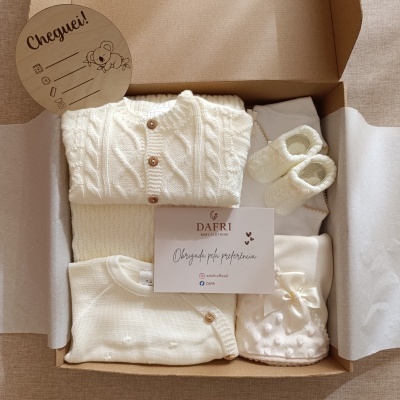 Caixa de roupa de bebé creme com camisola de malha, sapatinhos e manta