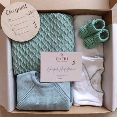 Conjunto de roupa de bebé em caixa com manta, camisola, body e botas de malha verde e azul, cartão e placa em madeira