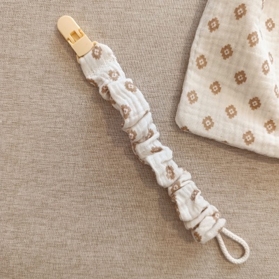 Prendedor de tecido branco com flores castanhas e fecho de plástico.