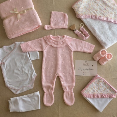 Conjunto de roupa de bebé em branco e rosa claro com macacão, body, calças, gorro, sapatinhos e manto.
