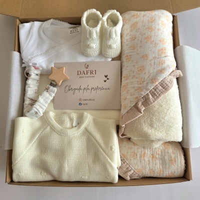 Kit de roupa de bebé em caixa com malha bege, body branco, sapatinhos brancos e tecido estampado