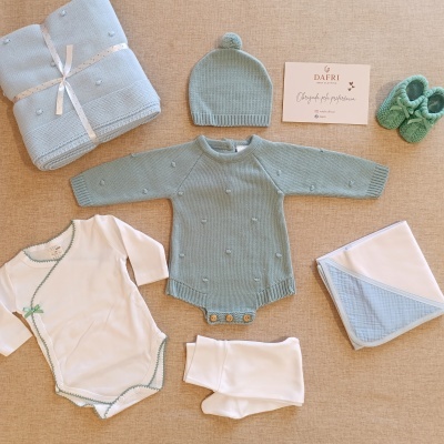 Conjunto de roupa de bebé com casaco, gorro, body, peúgas, sapatinhos, manta e lenço em tons azuis e brancos.