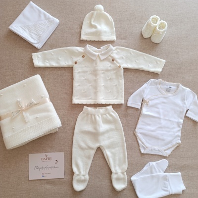 Conjunto de roupa de bebé branco com diferentes peças e cartão da marca DAFRI sobre fundo bege.