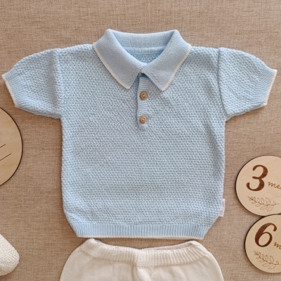 Conjunto de roupa de bebé azul e branca em malha e marcadores de idade em madeira sobre fundo bege