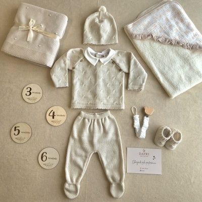 Conjunto de roupa de bebé bege em malha com vários acessórios e placas de madeira com idades, cartão de marca dafrí