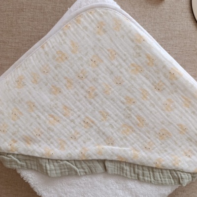 Toalha de bebé branca com padrão de coelhinhos cor de pêssego dobrada sobre fundo bege