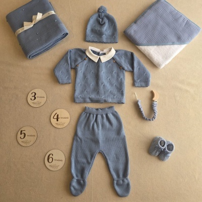 Conjunto de roupa de bebé em malha azul com acessórios em fundo bege.