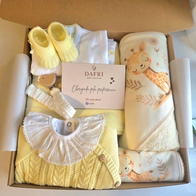 Conjunto de roupa de bebé com botas amarelas, body branco, camisola amarela, manta com estampa de girafa numa caixa de cartão