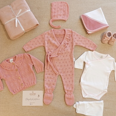 Conjunto de roupa de bebé em rosa e branco sobre tecido bege