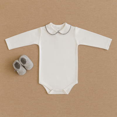 Body de bebé branco com gola decorada e sapatinhos cinza sobre fundo bege.