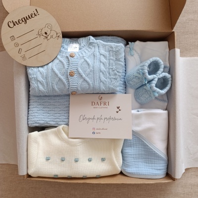 Conjunto de roupa para bebé azul e creme em caixa de cartão com etiquetas e cartão de agradecimento.