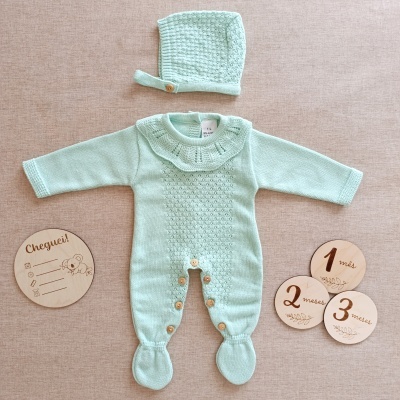 Macacão e gorro de bebé verdes com botões de madeira e discos de madeira com texto em português