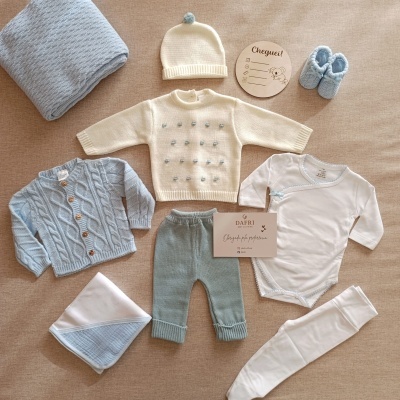 Conjunto de roupa de bebé azul e branca com vários acessórios e cartão DAFRI em fundo bege