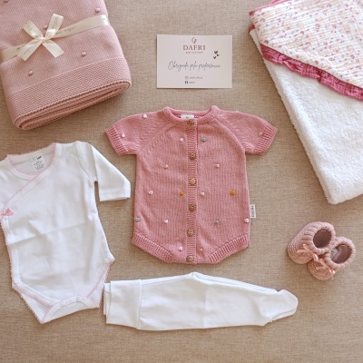 Conjunto de roupa de bebé com body branco, casaco rosa de malha, calças brancas, manta, sapatinhos cor-de-rosa e cartão da marca DAFRI