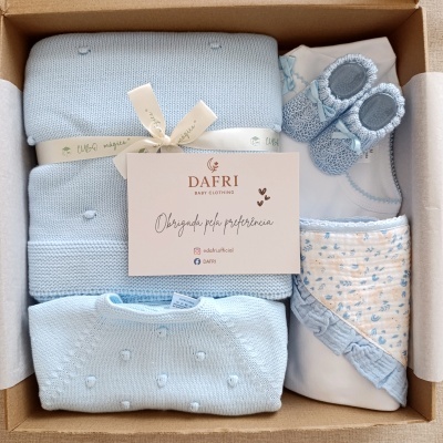 Conjunto de roupa para bebé azul e branco com manta, sapatinhos e babete numa caixa de cartão