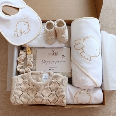 Conjunto de roupa e acessórios para bebé em tons bege e branco, com bordados de elefante, numa caixa de cartão.