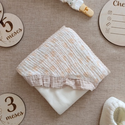 Fralda branca com padrão rosa e babado sobre superfície bege, com placas de madeira com números de meses