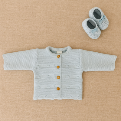 Conjunto de malha azul clara para bebé com camisola e sapatinhos sobre tecido bege