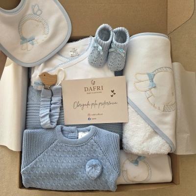 Conjunto de roupa para bebé com body, babete, sapatos de malha e manta em tons azuis e brancos numa caixa de cartão