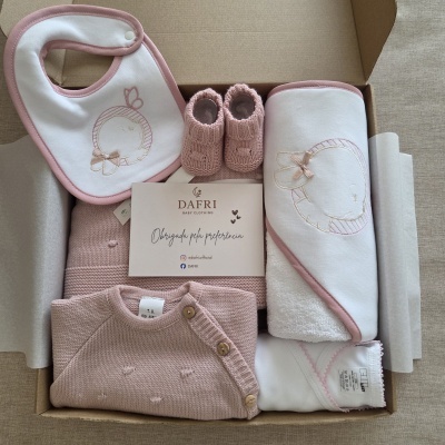 Conjunto de roupa de bebé rosa e branco com babete, sapatinhos, camisola e toalha num saco de cartão