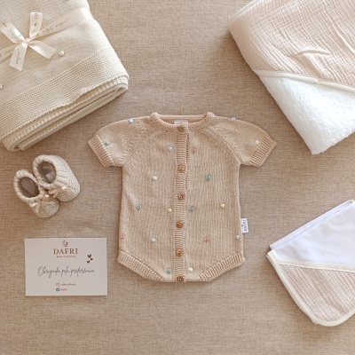 Conjunto de roupa e acessórios para bebé em tons bege e branco, com cartão da marca DAFRI